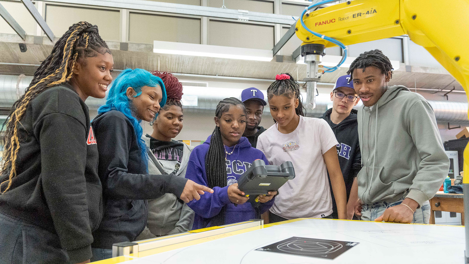 Students gather around a manufacturing robot.