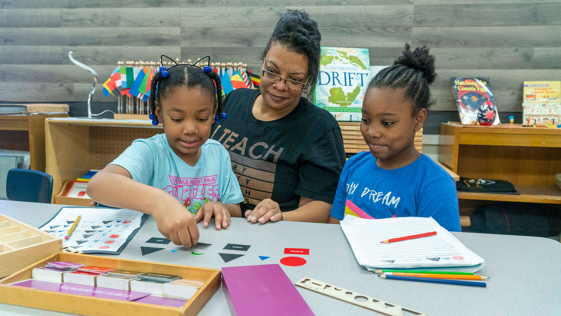 A teacher watches as two students learn shapes.