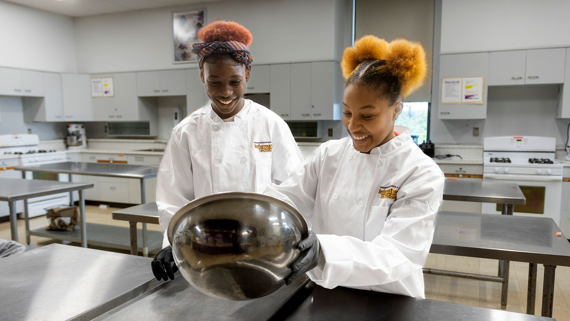 Two culinary students smile as they prepare food in a bowl.